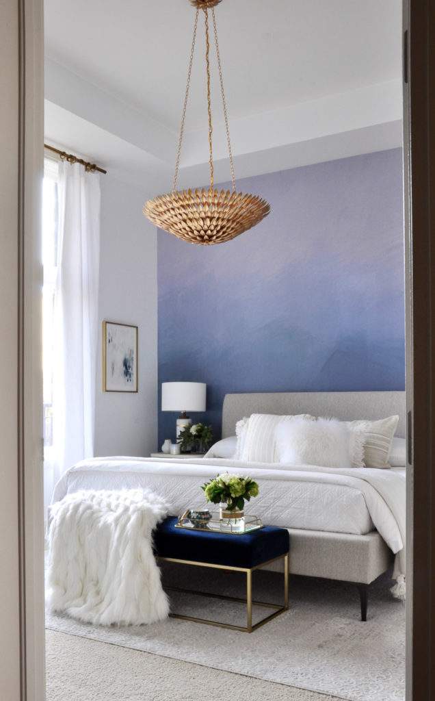 blue wall mural in bedroom with velvet bench at end of bed